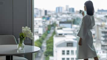 A room with a large window, a vase with flowers, and a person standing by the window.
