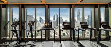 Un gimnasio con cintas de correr y elípticas, con amplias ventanas que ofrecen vistas a la ciudad.