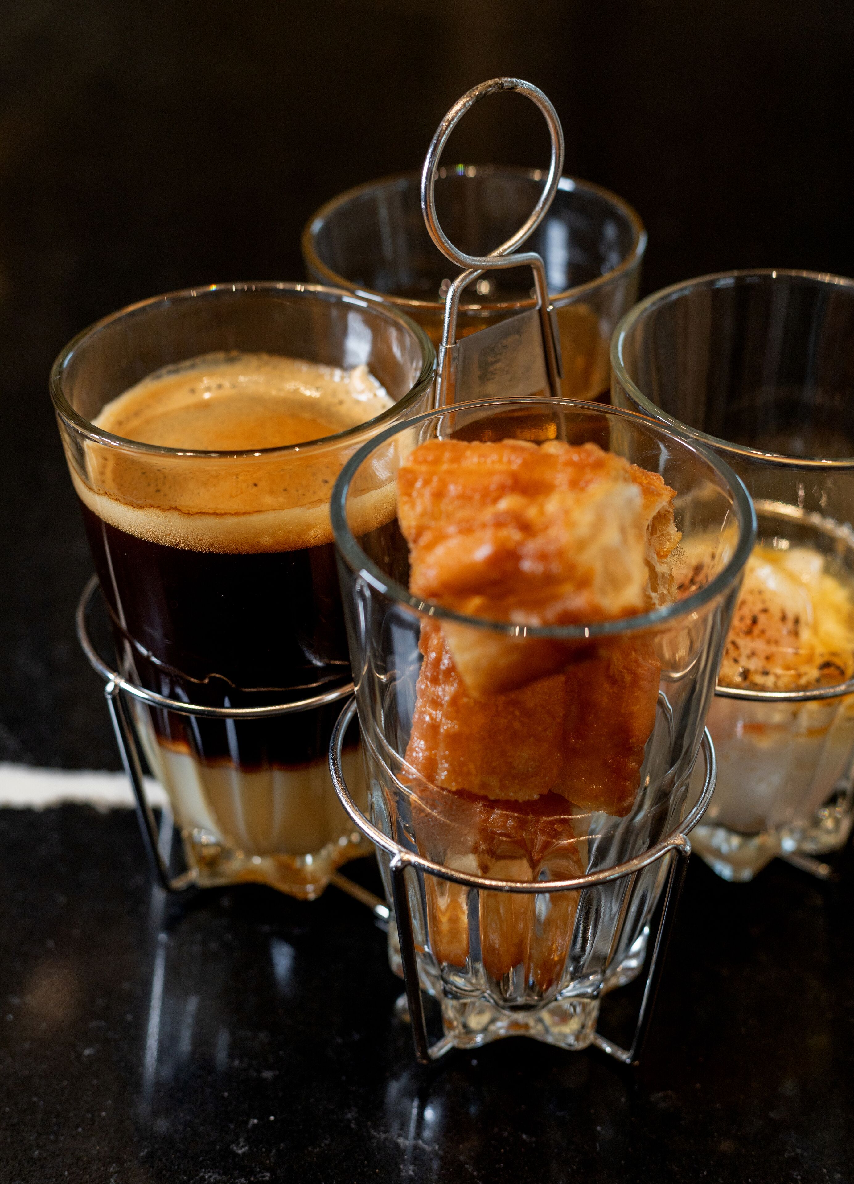 A close-up of four clear glasses with a metal coaster, each containing a different beverage.