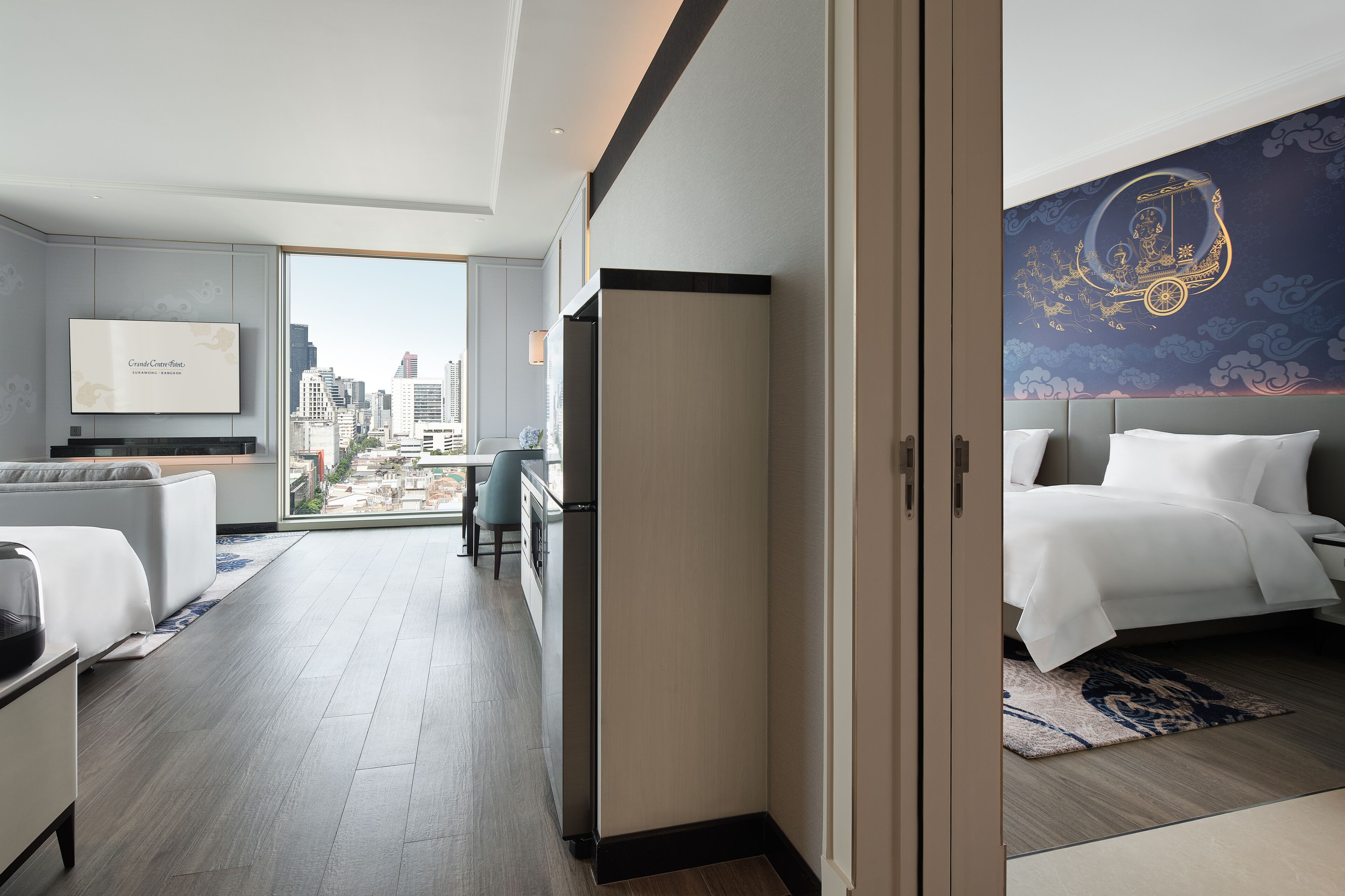 A modern hotel room with a city view, a large bed, a desk, and a television.