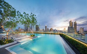Une piscine à débordement située sur le toit, offrant une vue panoramique sur la ville, et entourée d’arbres et de bâtiments modernes.