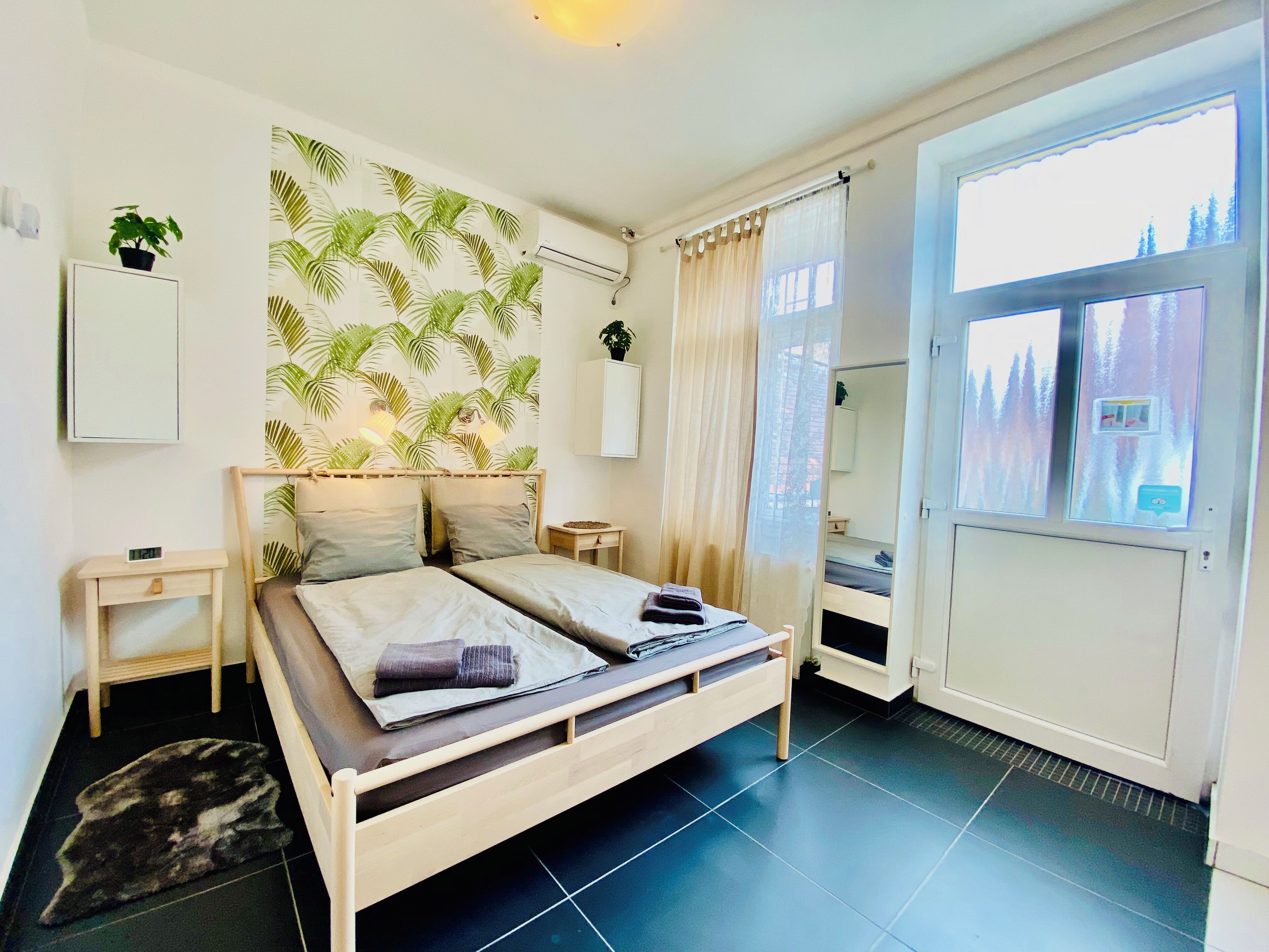 Une chambre à coucher avec un lit, des tables de chevet, un climatiseur fixé au mur, une plante en pot et une vue sur un paysage enneigé par la fenêtre.