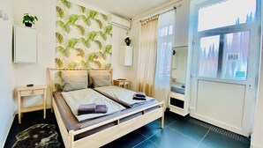 A bedroom with a bed, bedside tables, a wall-mounted air conditioner, a potted plant, and a view of a snowy landscape through a window. - Modern studio with city skyline view and A/C - Green Skyline Room (Budapest)