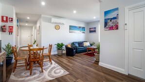 A modern living room with a dining area, featuring wooden furniture, a blue sofa, and a painting of a beach scene.