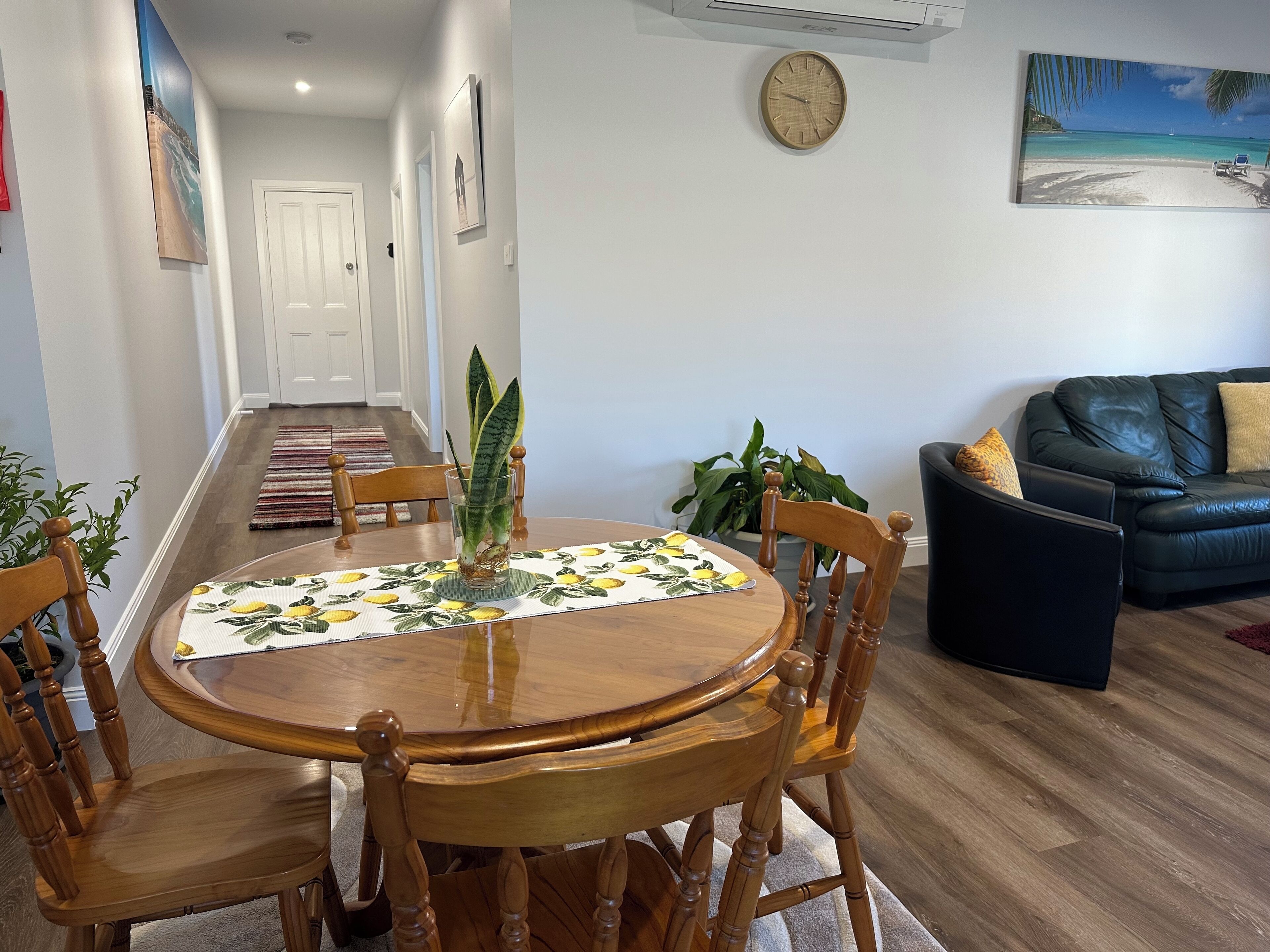 Un coin repas avec une table ronde en bois, des chaises, un vase avec une plante et un tableau accroché au mur.