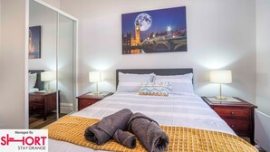 A hotel room with a bed, two bedside tables, a nightstand, a mirror, and a painting of a bridge and moon.