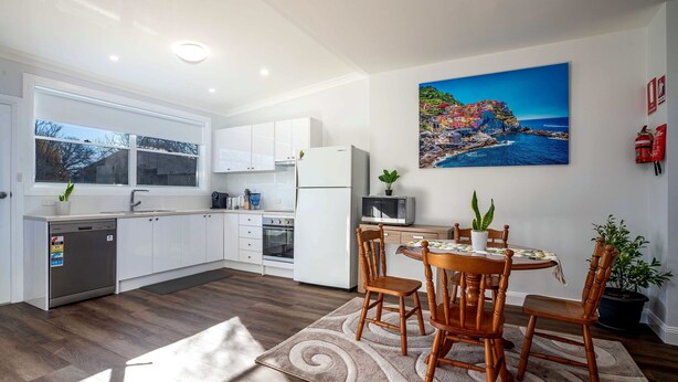 A modern kitchen with white cabinets, a built-in oven, and a dining area with a wooden table and chairs.