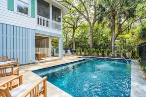 A swimming pool with a wooden deck and lounge chairs, surrounded by trees and a fenced area. - Chasing Waves | Heated Pool | 3 Min Beach (Edisto Island)