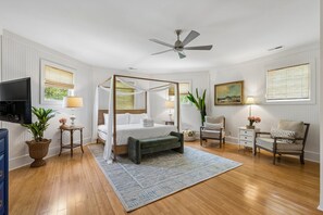 Une chambre à coucher avec un lit à baldaquin, un ventilateur de plafond, une télévision et une grande fenêtre donnant sur un paysage verdoyant.