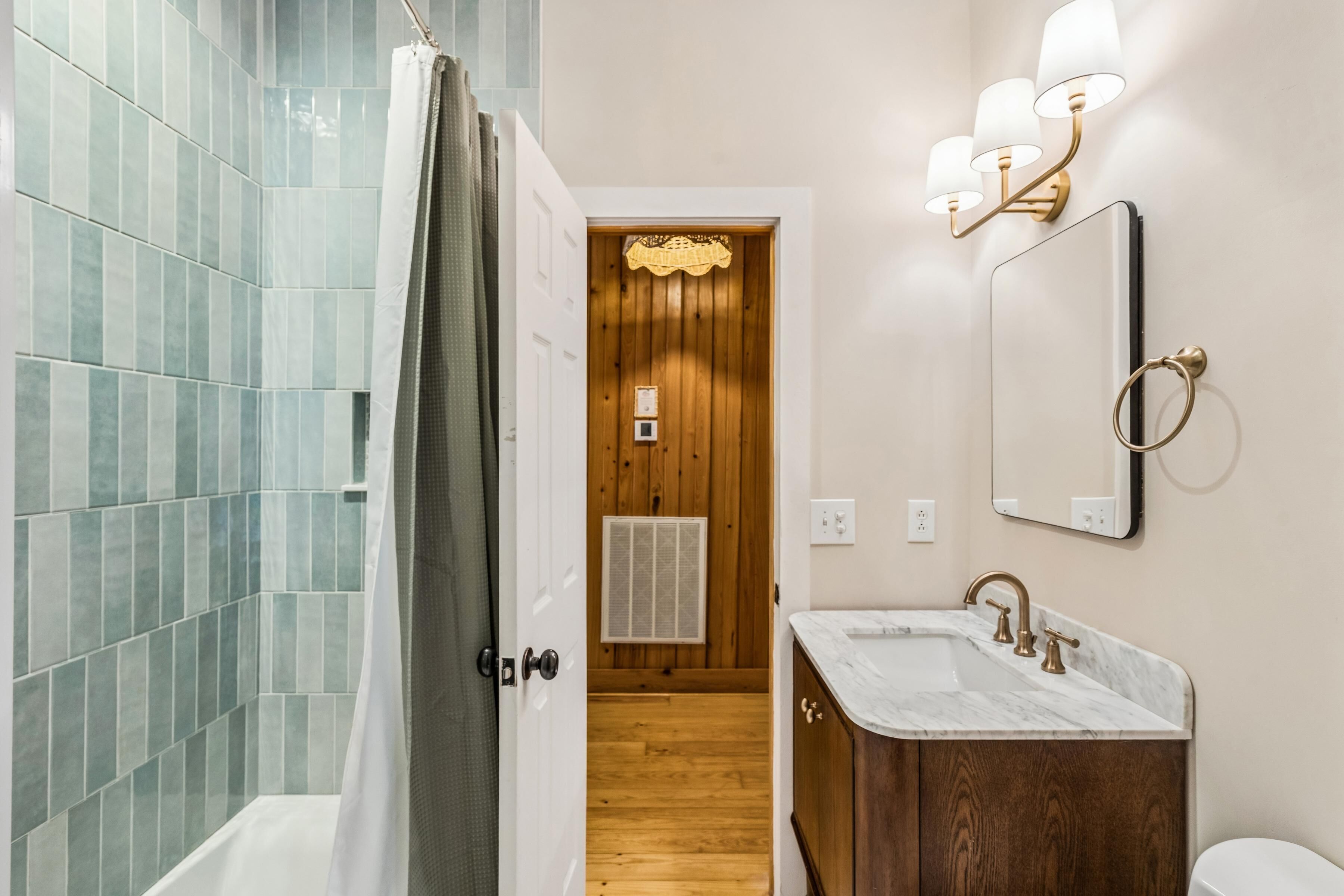A bathroom with a shower, a sink with a mirror, and a wooden door.