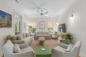 Un salon comprenant un canapé, deux fauteuils, une table basse, un téléviseur et un ventilateur de plafond.