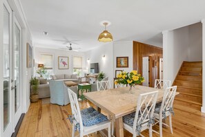 A spacious living area with a wooden dining table, white chairs, and a staircase. - Chasing Waves | Heated Pool | 3 Min Beach (Edisto Island)