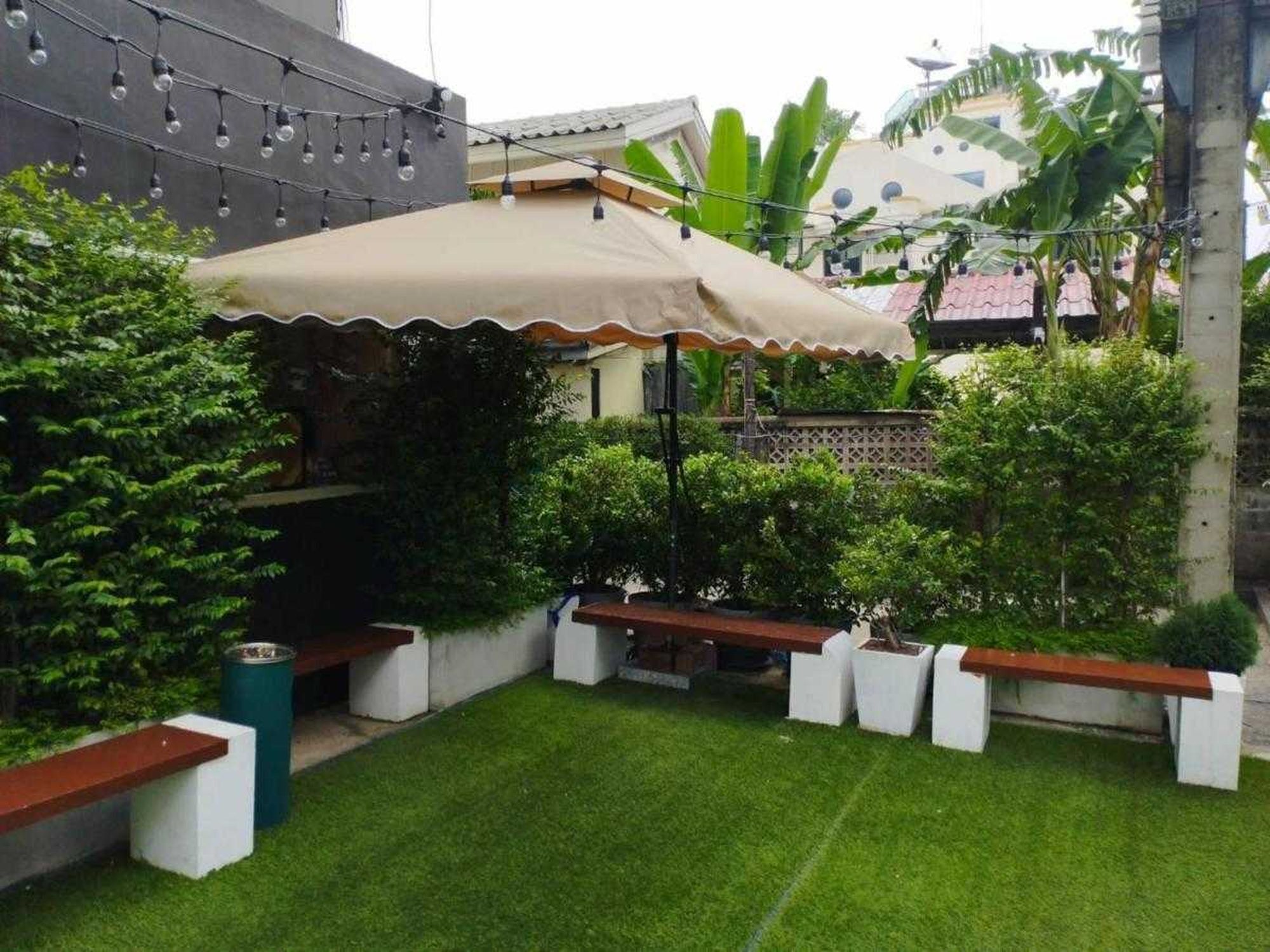 En patio med overdækket siddeområde, lyskæde og velplejet græsplæne.