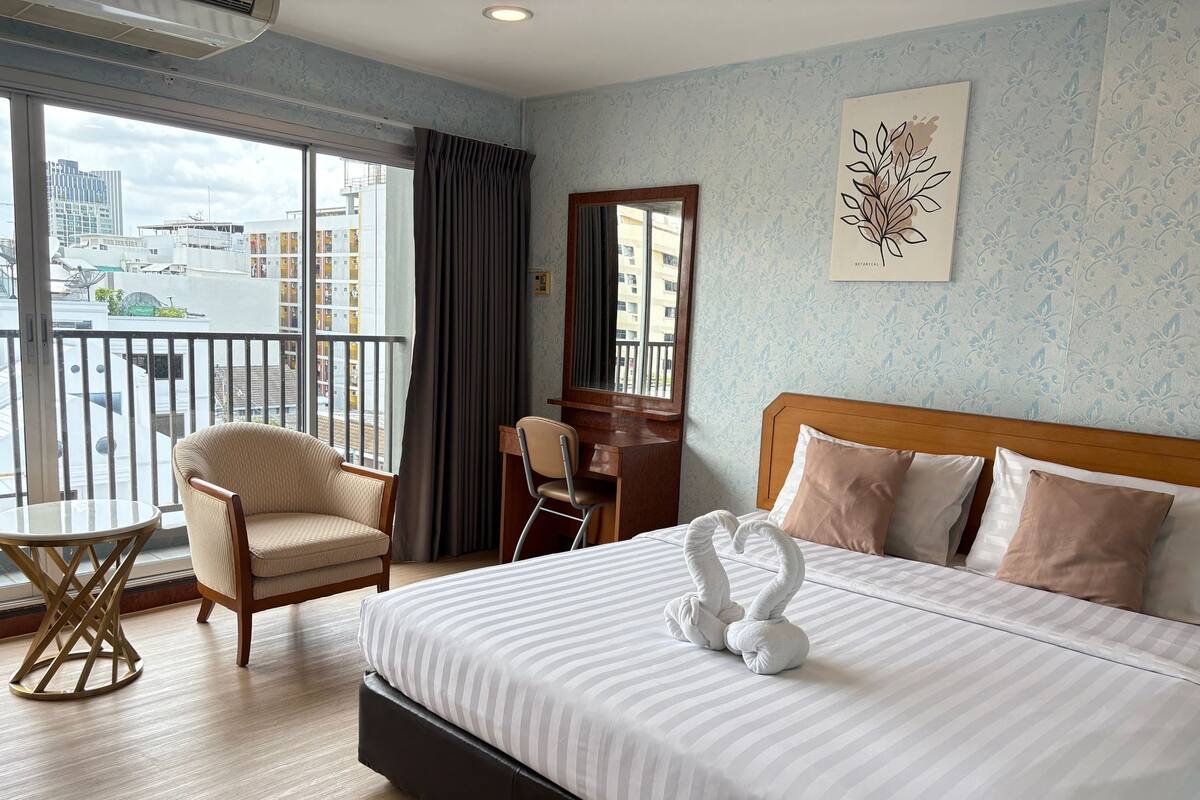 A hotel room with a large bed, a desk, a chair, and a view of the city through the balcony.