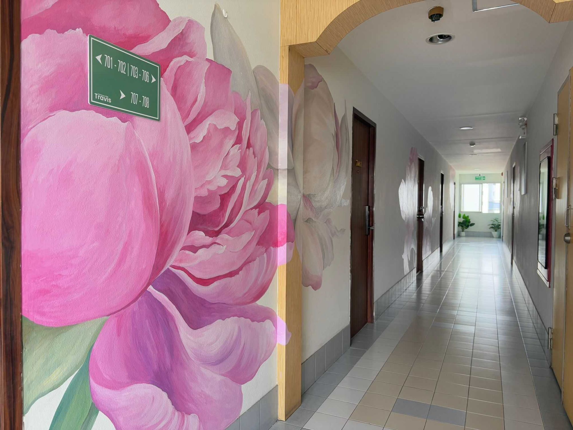 Un pasillo con un gran mural floral en la pared, una señalización verde direccional y un piso de baldosas.
