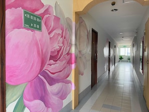 A hallway with a large floral mural on the wall, a green directional sign, and a tiled floor. - OYO 75446 Travis Inthamara 49 (Bangkok)