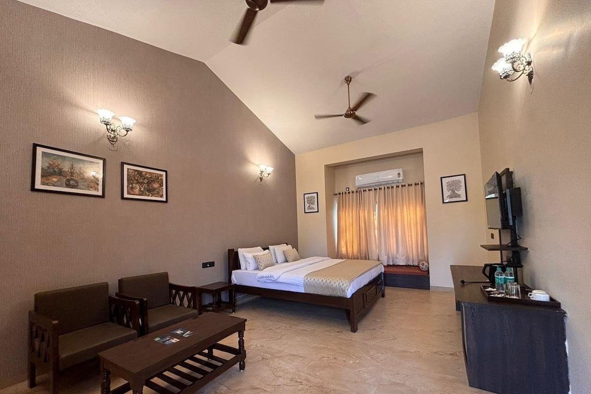 A hotel room with a bed, a desk, a chair, a coffee table, a ceiling fan, and wall-mounted lights.
