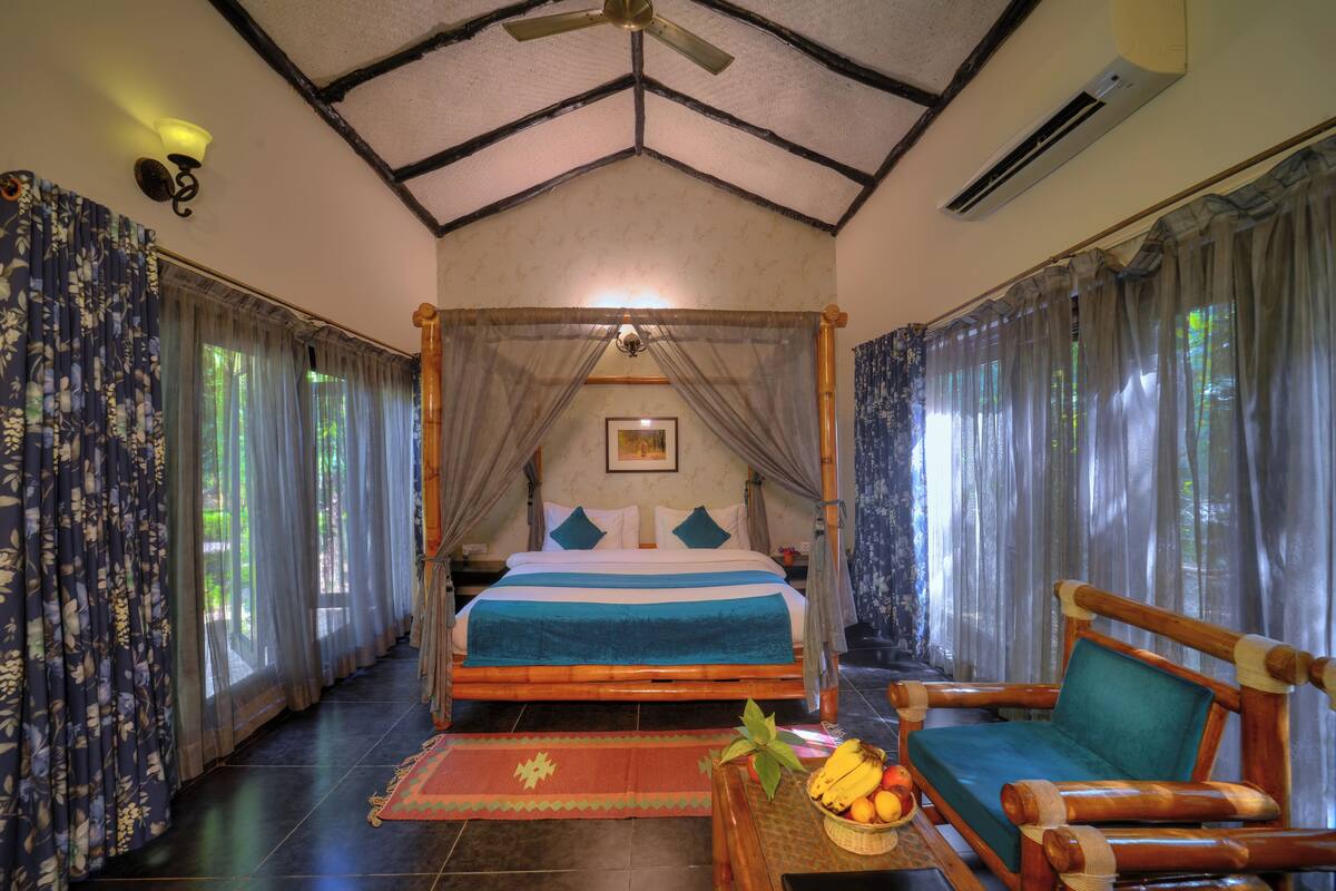 A four-poster bed with a canopy, a wooden chair with a cushion, and a fruit basket on a table.
