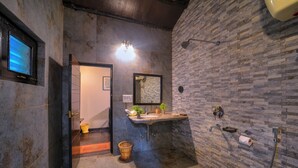 Un baño con pared de piedra, lavabo, espejo, ducha y ventana.