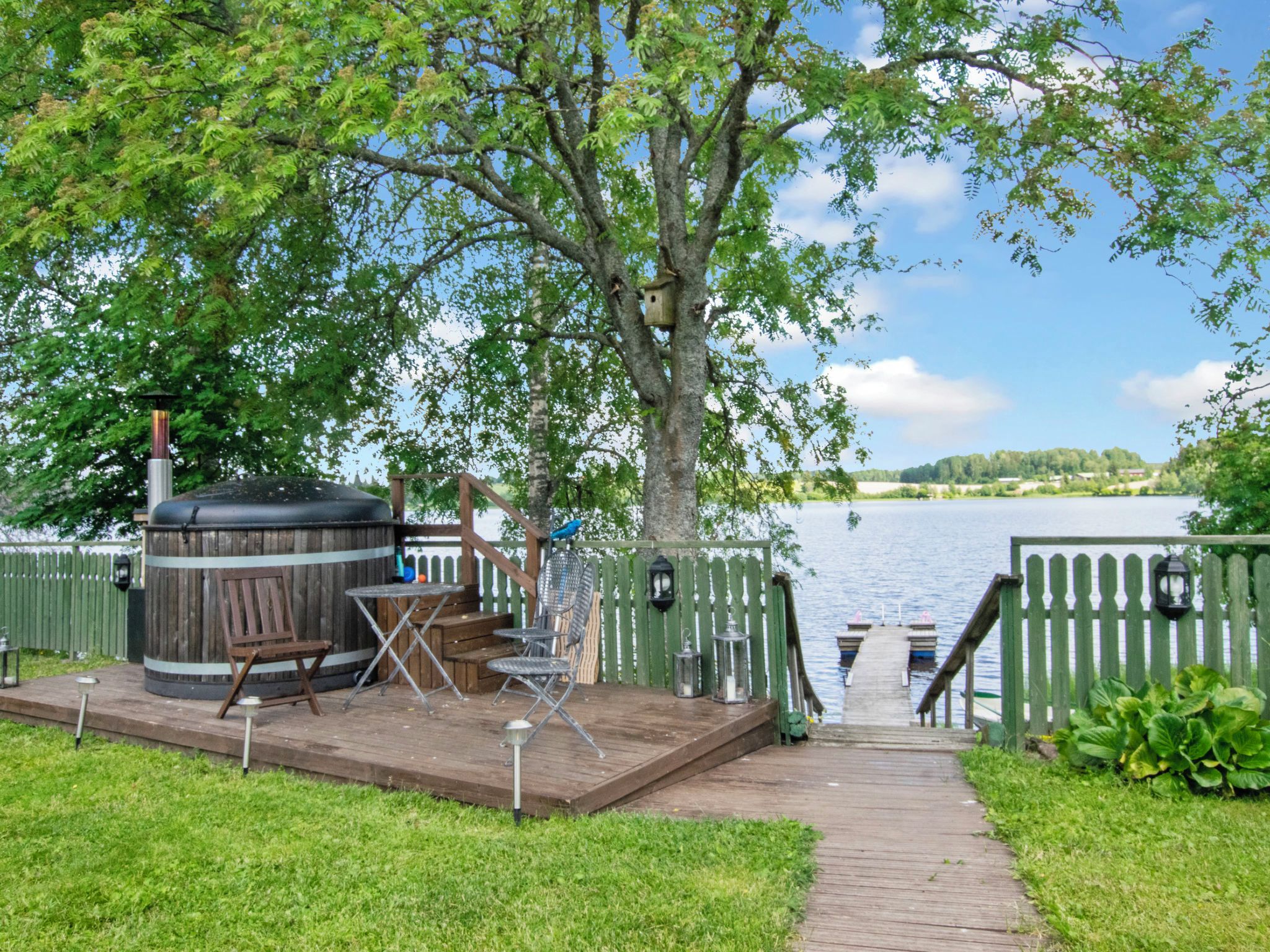 Eine Holzterrasse mit Gartenmöbeln, einem Whirlpool und Blick auf einen See.