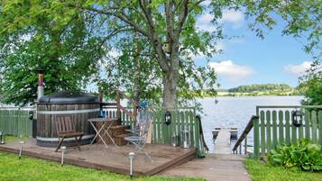 Eine Holzterrasse mit Gartenmöbeln, einem Whirlpool und Blick auf einen See.
