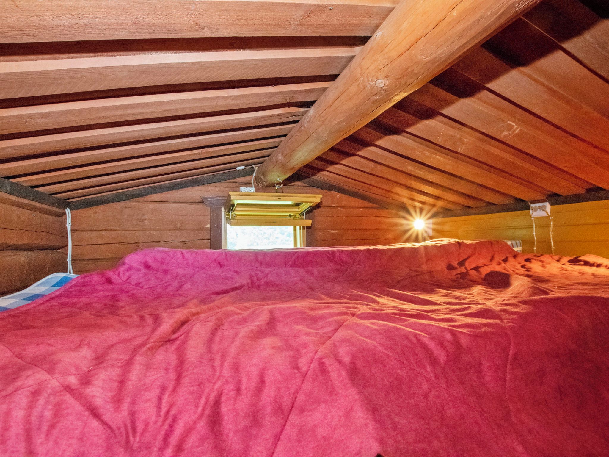 A room with a sloped ceiling, a bed with a pink blanket, and a small table with a lamp.