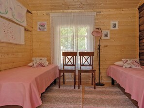 A room with two wooden beds, a lace curtain, and a floor lamp.