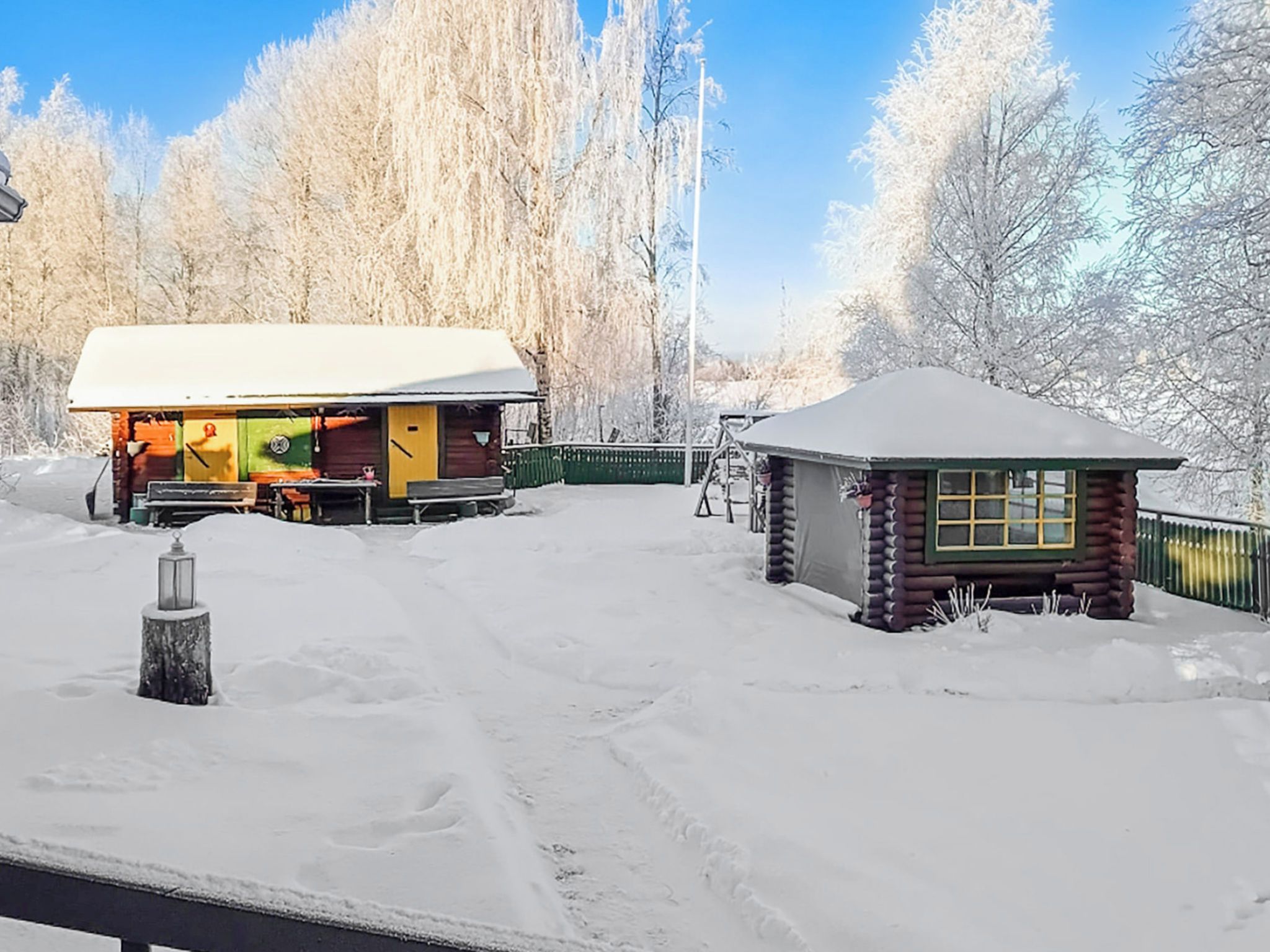 Eine Hütte mit schneebedecktem Dach und einem kleinen Anbau, umgeben von verschneiter Landschaft und Bäumen.