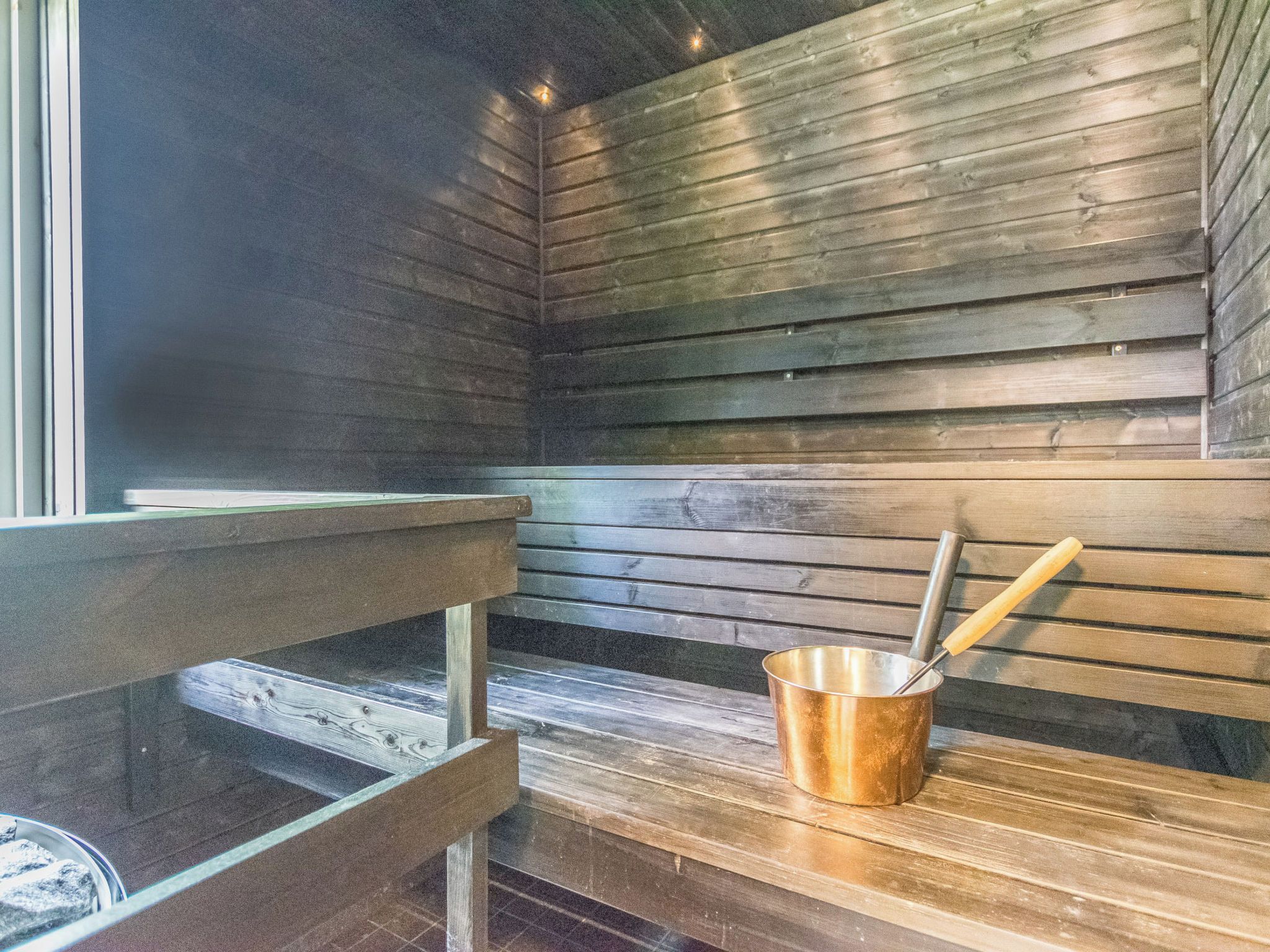Een sauna met houten banken en een metalen emmer met een schaal.