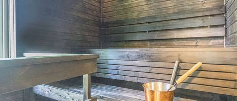 Een sauna met houten banken en een metalen emmer met een schaal.