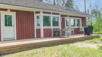 A single-story building with a red exterior, white trim, and a tiled roof. There is a covered outdoor seating area with a table and chairs, and a grill.