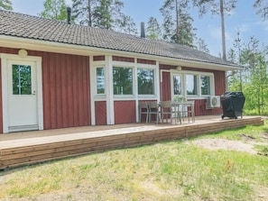 Yhden kerroksen rakennus, jonka ulkoseinät ovat punaiset, reunalistat valkoiset ja katto on laatoitettu. Siinä on katettu ulkotila, jossa on pöytä ja tuoleja sekä grilli.