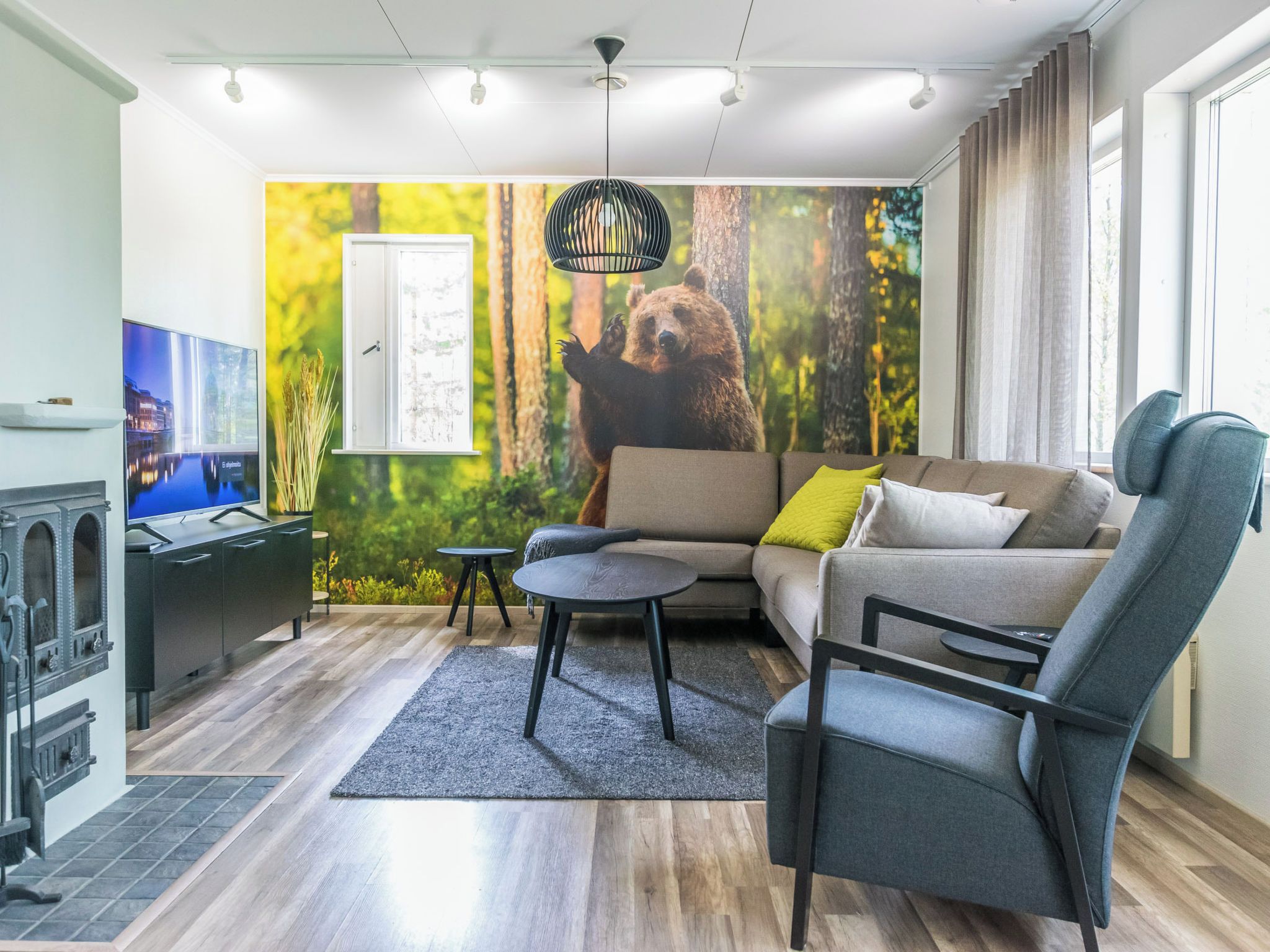 A modern living room with a sofa, a chair, a small table, a television, and a mural of a bear in a forest.