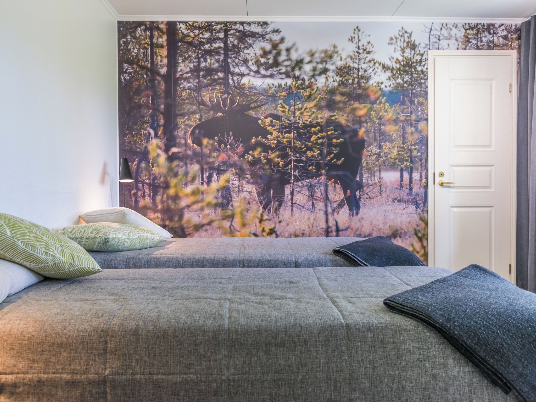 Una camera da letto con un grande affresco raffigurante una foresta, un letto con biancheria grigia e una porta con maniglia.