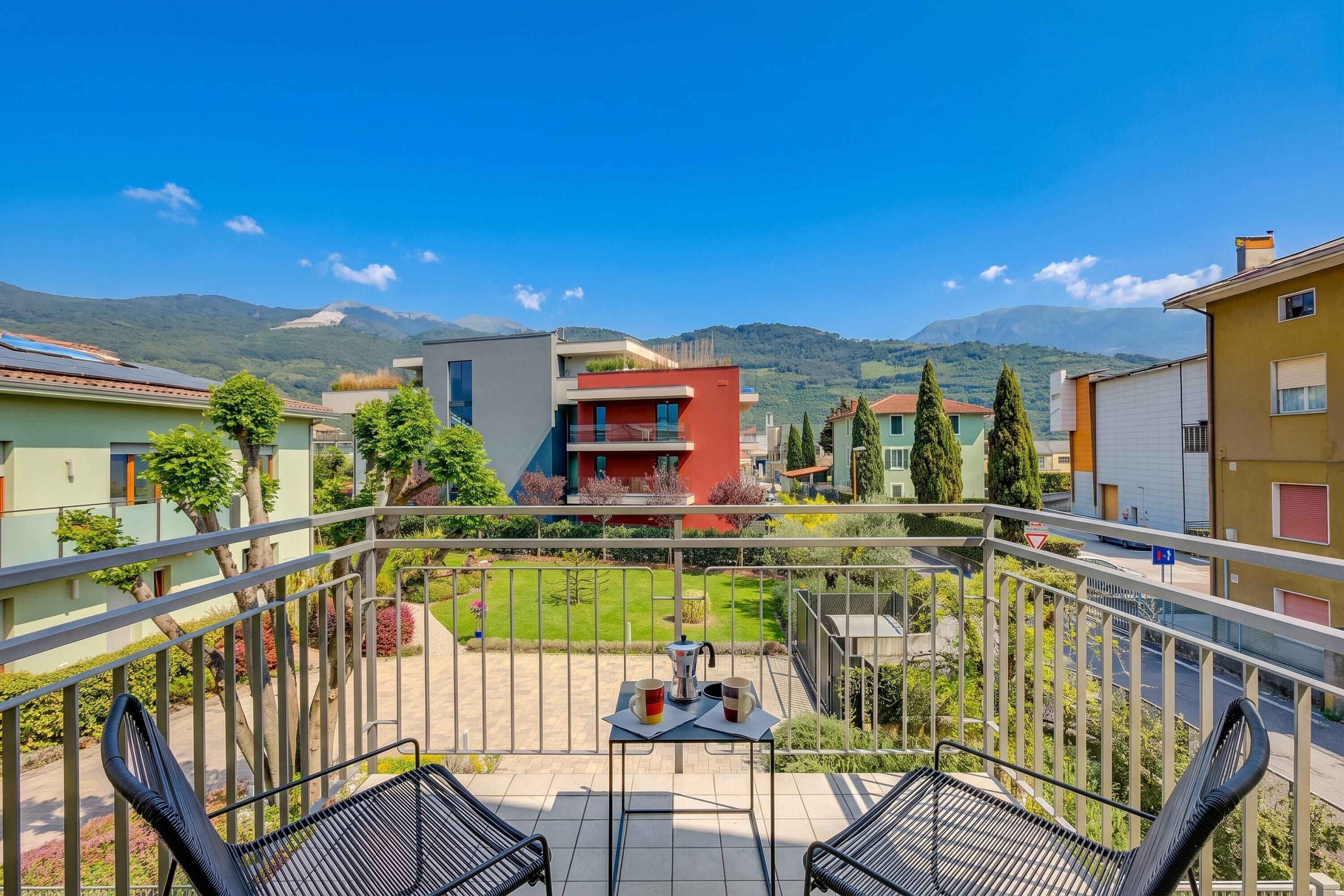 A balcony with a table and chairs, a view of a green landscape, and buildings in the background.