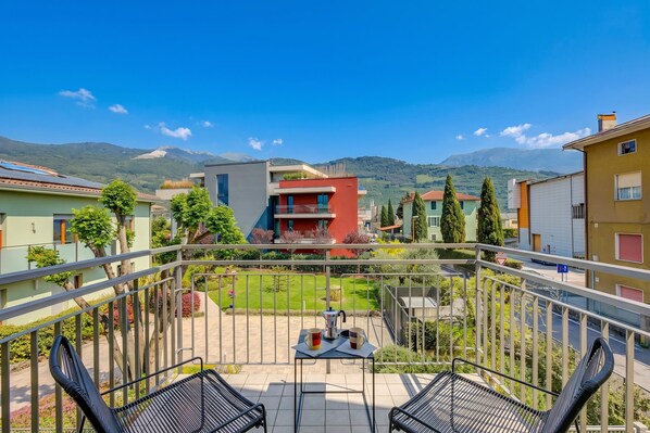 A balcony with a table and chairs, a view of a green landscape, and buildings in the background.