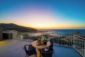 Une terrasse avec une table dressée pour le dîner, offrant une vue sur un paysage côtier au coucher du soleil.