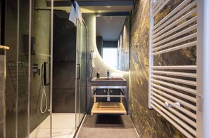 Une salle de bain moderne dotée d’une douche à parois de verre, d’un mur recouvert de carreaux de marbre, d’un lavabo encastré et d’un porte-serviettes.