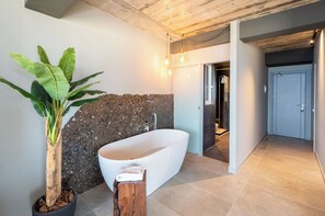 Ein modernes Badezimmer mit einer freistehenden Badewanne, einer großen Kübelpflanze und einem hölzernen Hocker.
