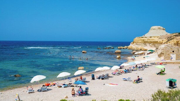 A beach with clear blue water, white umbrellas, and people relaxing. - Salini Suites Luxury Accommodation with Corner Terrace and Deck Area 501 (Iż-Żebbuġ)