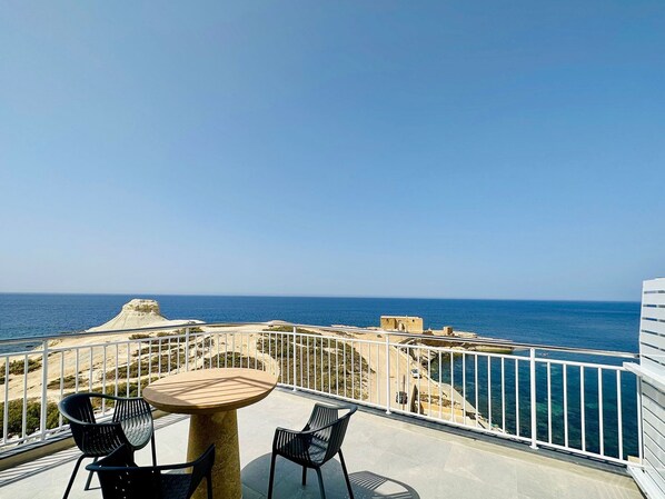 A balcony with a table and chairs overlooking the sea.