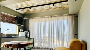 A modern living room with a wooden dining table, green chairs, a yellow armchair, and a balcony with sheer curtains. - Salini Suites Luxury Accommodation with Corner Terrace and Deck Area 501 (Iż-Żebbuġ)
