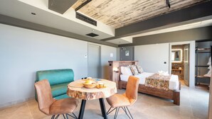 A modern hotel room with a bed, a green sofa, a round wooden table with chairs, and a bathroom visible through an open door. - Salini Suites Luxury Accommodation With Terrace and Sea View 101 (Iż-Żebbuġ)