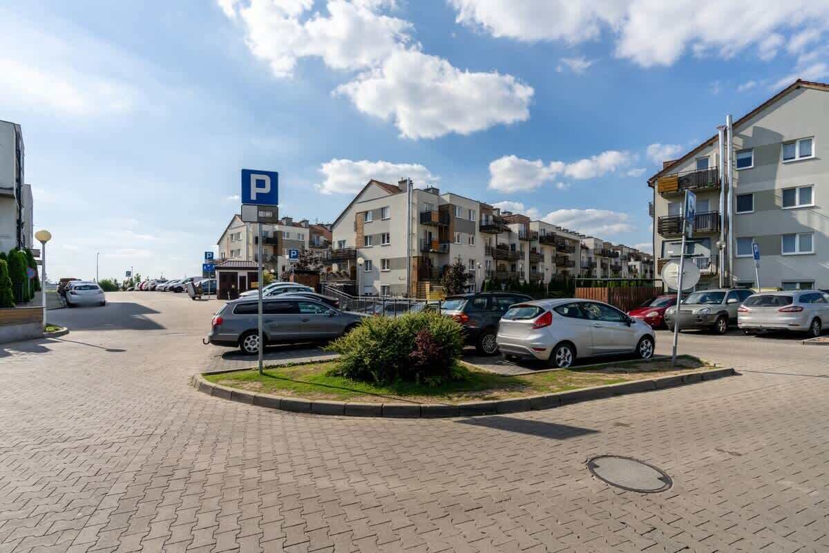 Ein Parkplatz mit mehreren Autos, einem blauen Parkschild und Wohnhäusern im Hintergrund.