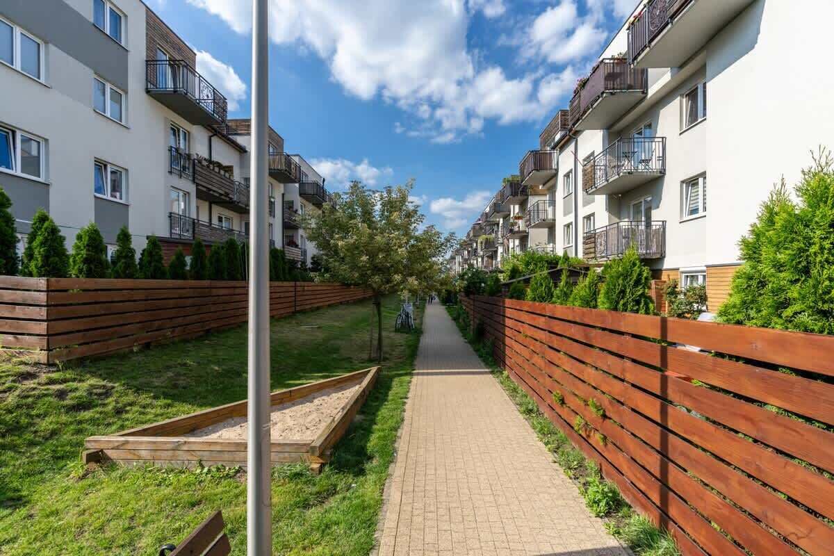 A residential building with multiple balconies, a paved pathway, and a wooden fence.
