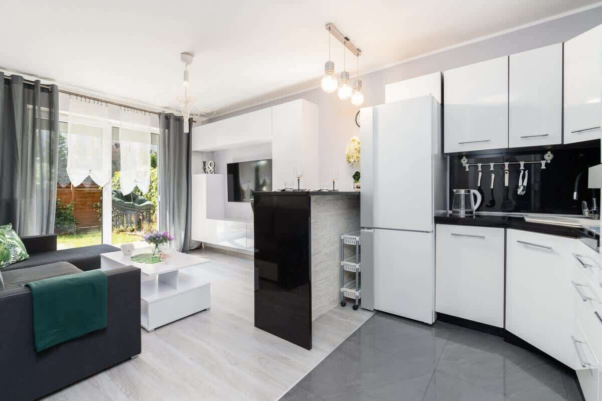 Eine moderne Küche mit weißen Schränken, einem schwarzen Kühlschrank und einem Essbereich mit weißem Tisch und einer Couch.