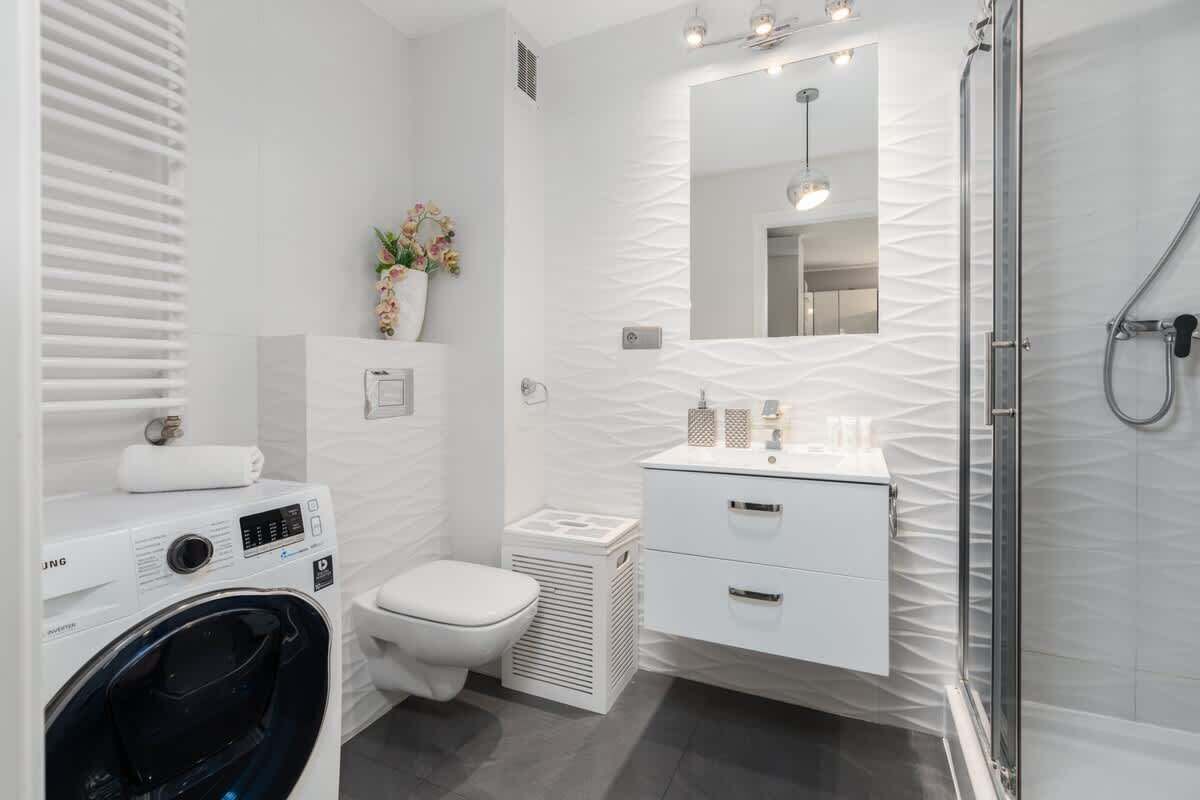 Un bagno moderno con lavatrice, servizi igienici e zona doccia con pareti in vetro.