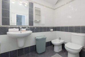 A bathroom with a white sink, a bidet, a toilet, and a trash bin.