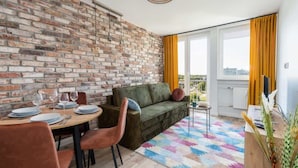 A dining area with a brick wall, a green sofa, and a colorful rug. - Elegant Apartment in Wroclaw | Close to Main Railway Station (Wroclaw)