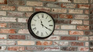 A brick wall with a clock, a table set with plates and glasses, and a cushioned chair. - Elegant Apartment in Wroclaw | Close to Main Railway Station (Wroclaw)
